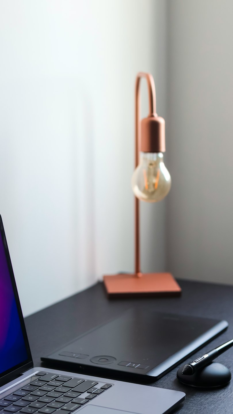 Notebook, grafický tablet a stolná lampa na pracovnom stole.